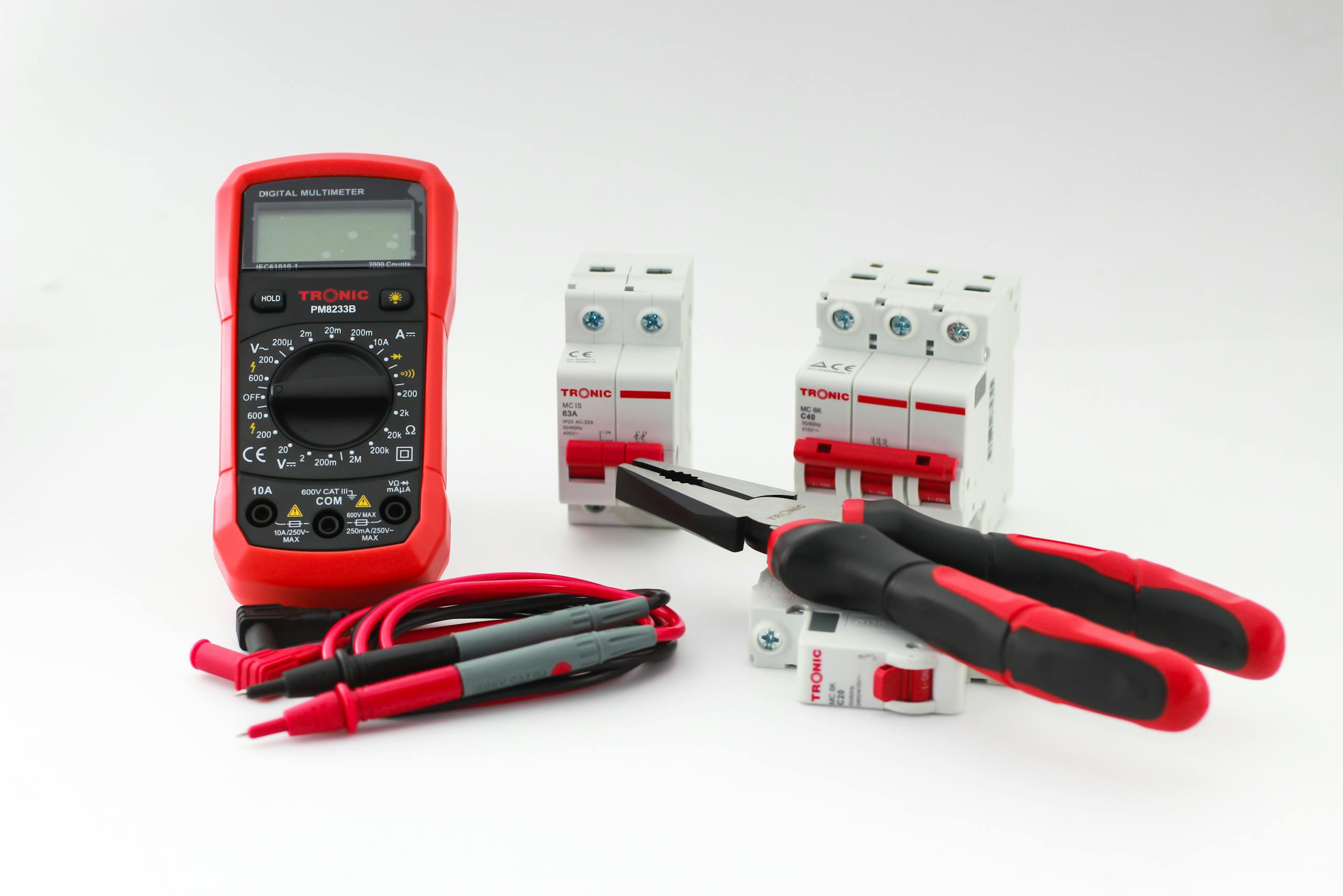 Close-up of a digital multimeter with electrical tools and circuit breakers on a white background.